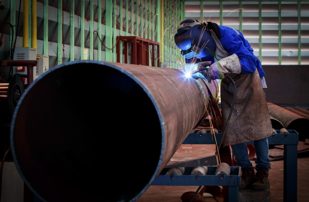 A pipe fabricator working in a fabrication shop with overhead cranes and hoists, a variety of hand tools, grinders and cutting equipment.