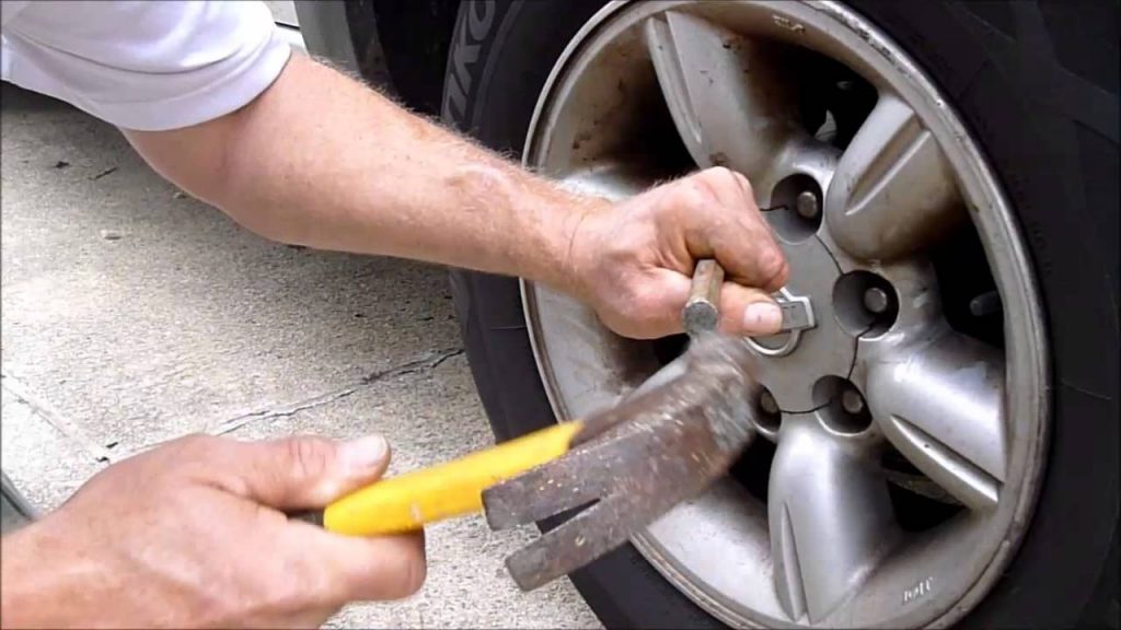 A man using hammer and socket to remove a stuck lug nut