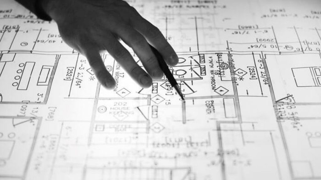 a hand with a pen pointing into a blueprint