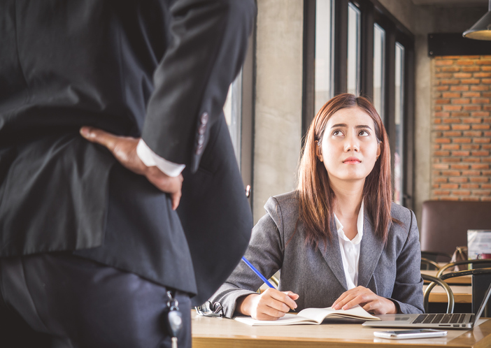 woman in unhappy job wearing business suit looking up at suited man in trendy office